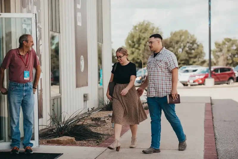 A greeter holding the door as a couple walks in